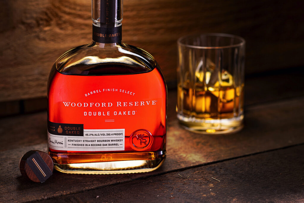 Warmly lit bottle of Woodford Reserve with a glass on the rocks